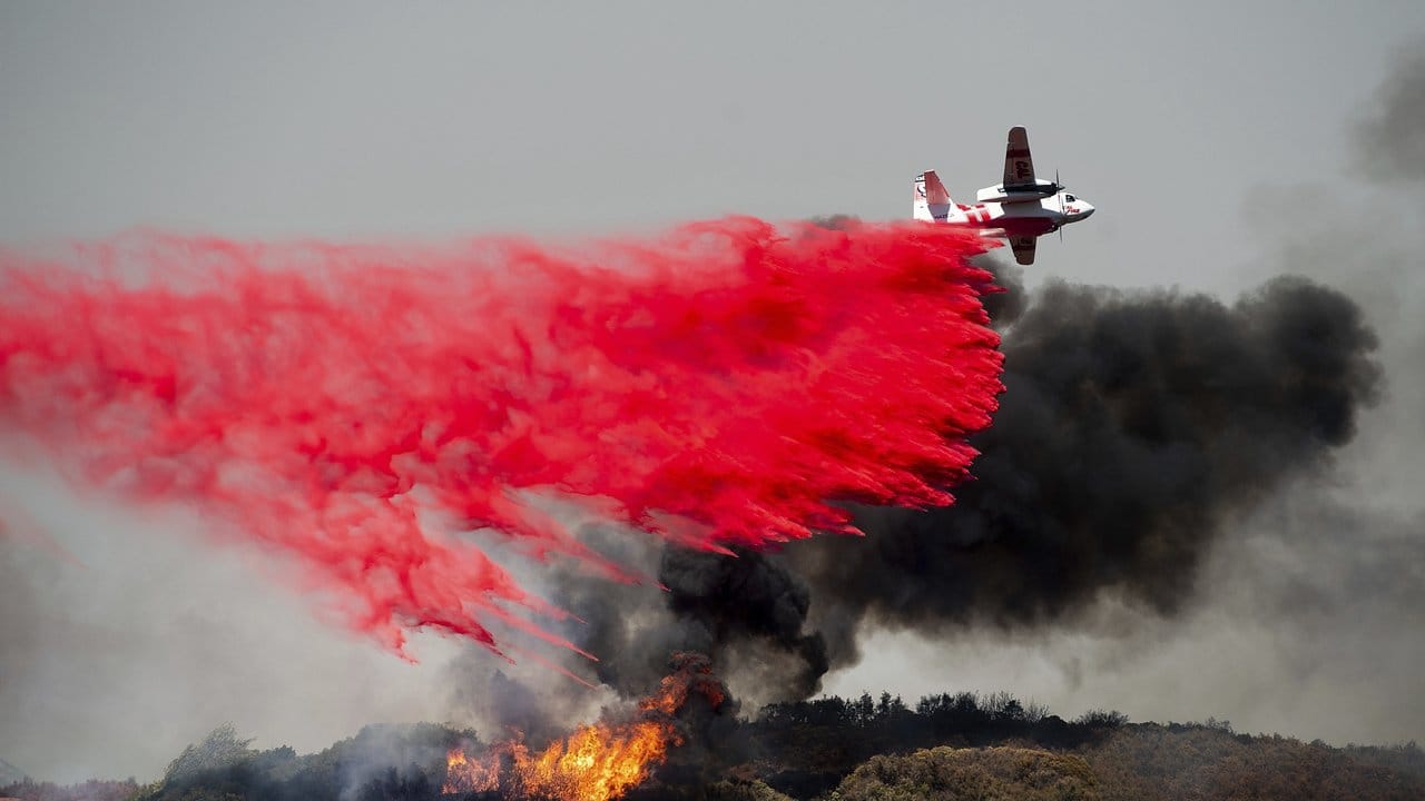 Ein Flugzeug lässt Löschmittel auf einen Waldbrand fallen. Ein Flugzeug lässt Löschmittel auf einen Waldbrand fallen.