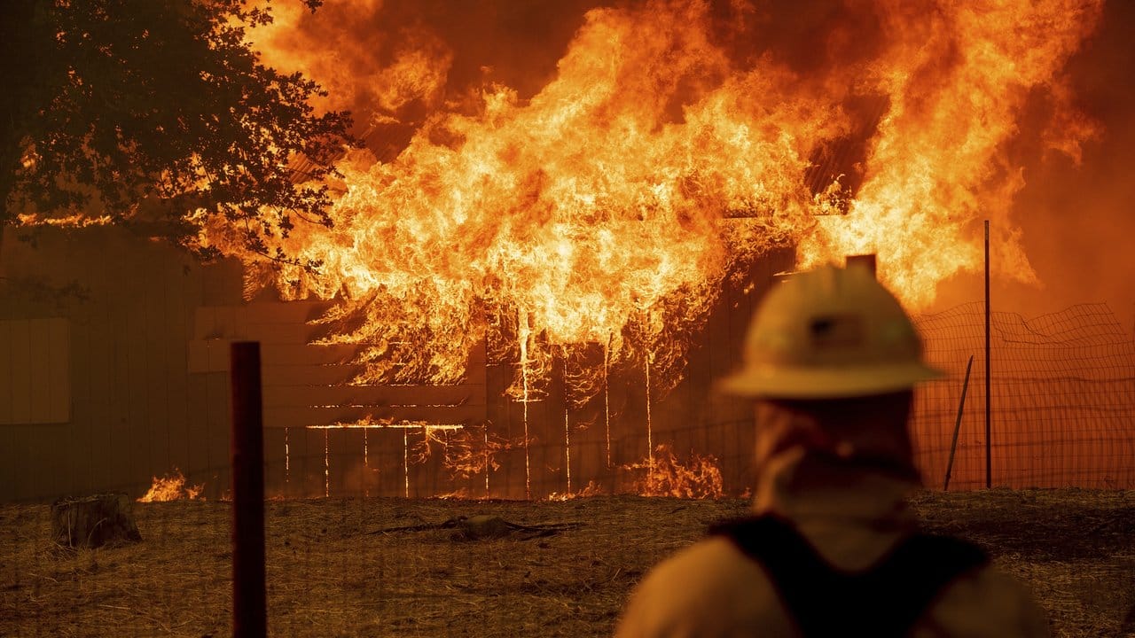 Ein Feuerwehrmann überwacht ein brennendes Gebäude, um sicherzustellen, dass sich die Flammen nicht ausbreiten. Ein Feuerwehrmann überwacht ein brennendes Gebäude, um sicherzustellen, dass sich die Flammen nicht ausbreiten.
