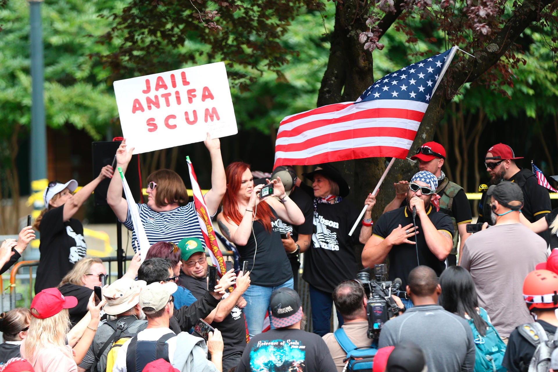 Unter den Anhängern der rechtsextremen Gruppe Patriot Prayer hält eine Frau ein Schild mit einem Schriftzug gegen die Linken hoch: "Jail Antifa Scum" (deutsch: "Ins Gefängnis mit dem Antifa-Abschaum"): Die Linken hatten zu Gegendemonstrationen aufgerufen.