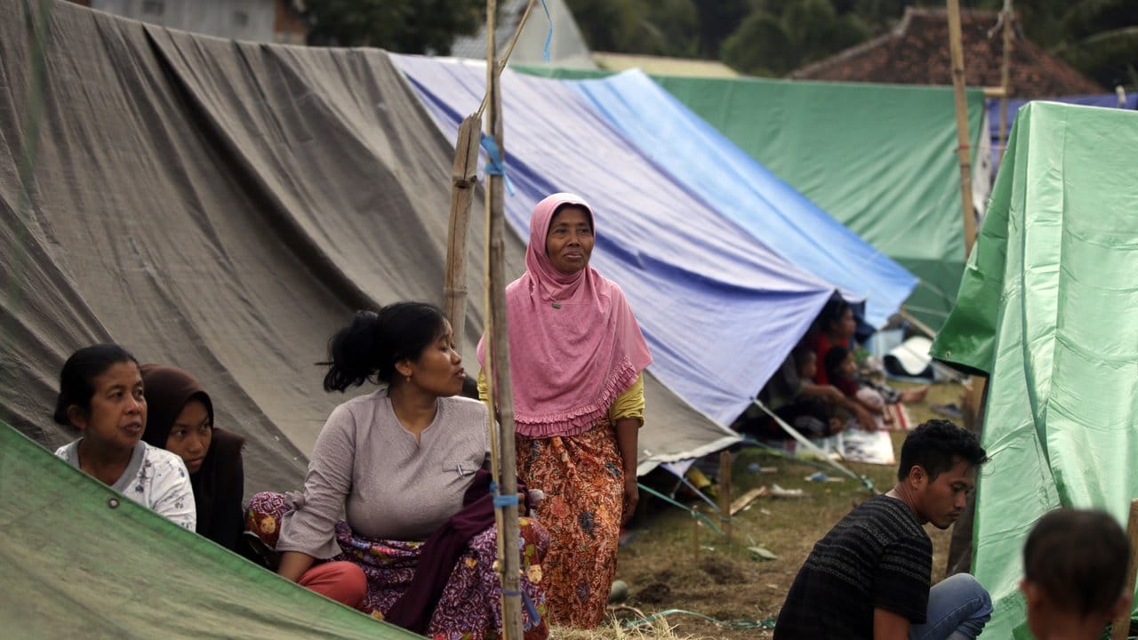 Übernachten im Freien: Dorfbewohner vor Zelten in einem provisorischen Unterstand.