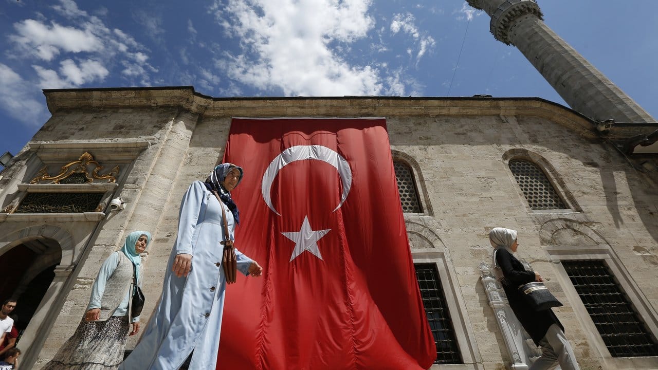 Frauen gehen in Istanbul an einer Moschee vorbei, an der eine große türkische Fahne hängt.