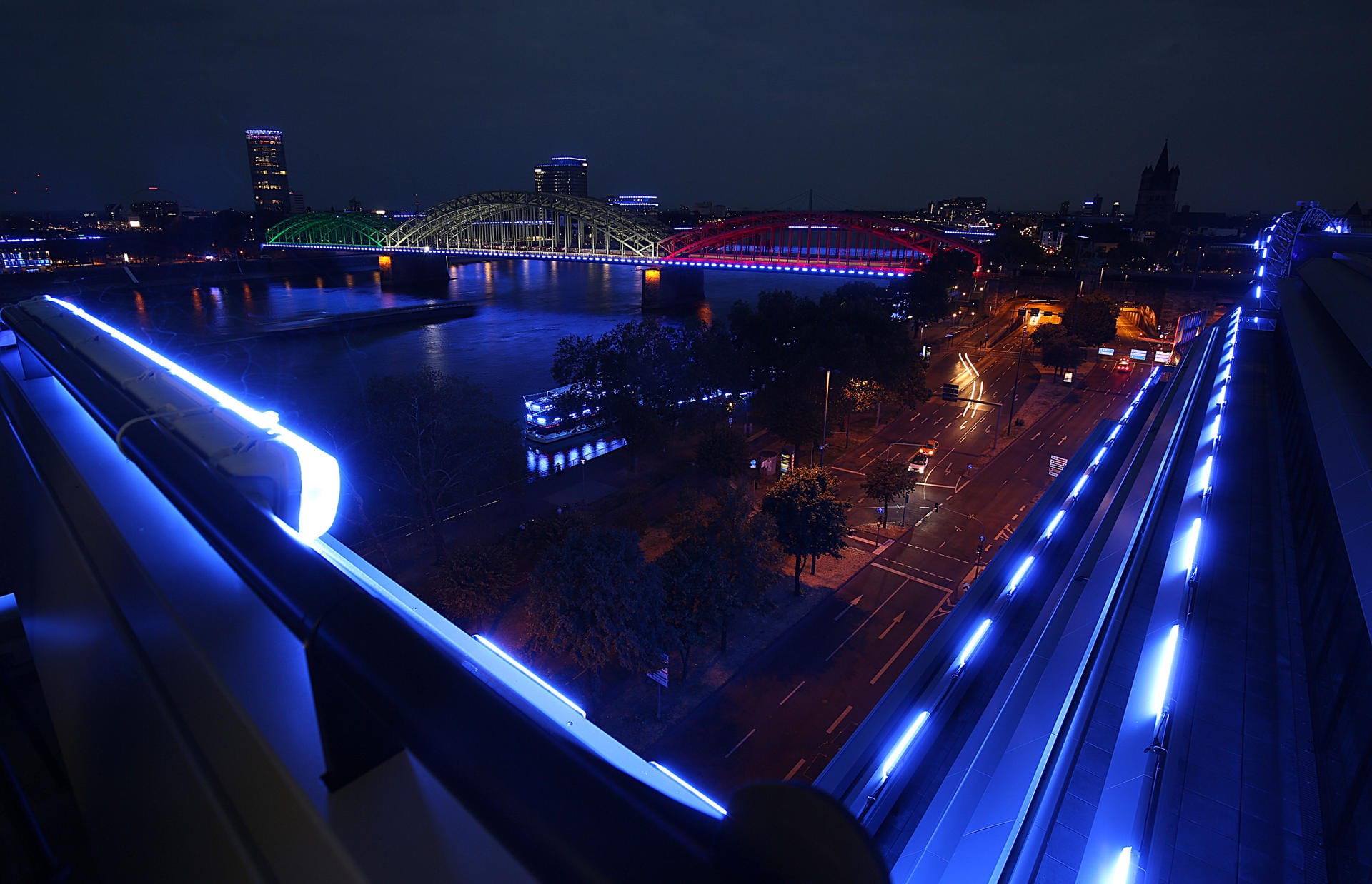 Gebäude am Rheinufer und die Hohenzollernbrücke sind illuminiert. Zum zehnjährigen Jubiläum der Computerspielemesse Gamescom wird jeden Abend während der Messe das Kölner Rheinufer mit 7.000 Leuchtstoffröhren beleuchtet.