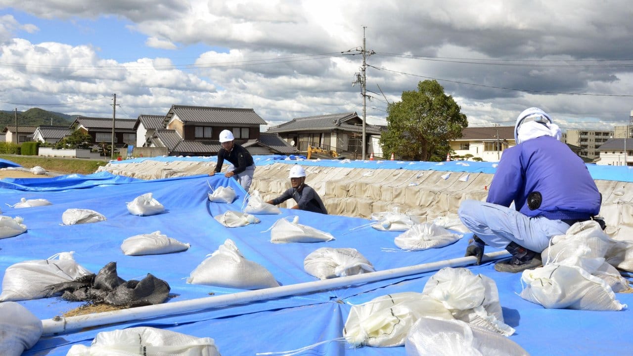 Arbeiter legen Sandsäcke über blaue Planen in Vorbereitung auf den herannahenden Taifun.