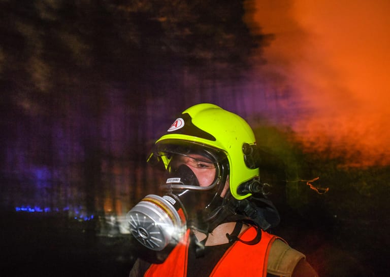 Mit Atemschutzmaske kommt ein Feuerwehrmann aus einem brennenden Waldstück. Bewohner der umliegenden Dörfer und Städte sollen sich ebenfalls vor dem Rauch schützen.
