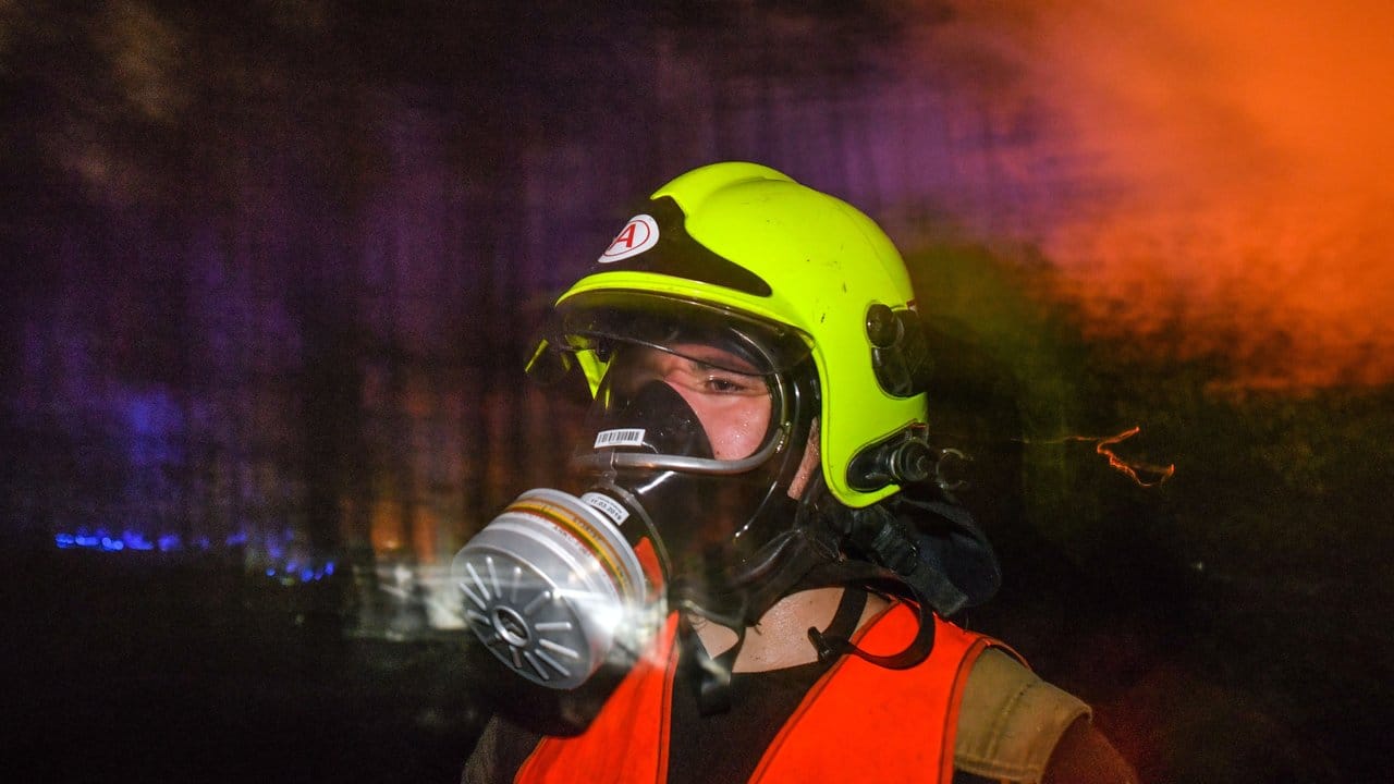 Mit Atemschutzmaske kommt ein Feuerwehrmann aus einem brennenden Waldstück. Mit Atemschutzmaske kommt ein Feuerwehrmann aus einem brennenden Waldstück.