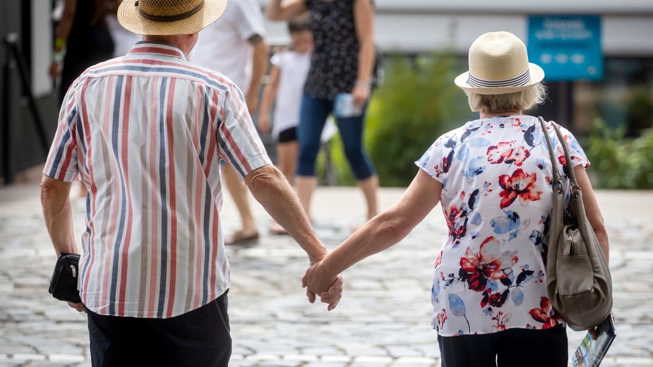 Zwei ältere Menschen mit überqueren Hand in Hand einen Fußgängerüberweg.