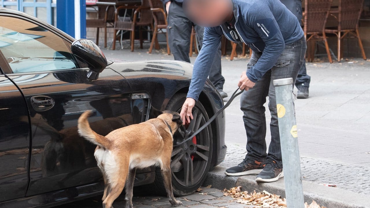 Ein Polizist untersucht mit einem Spürhund ein verdächtiges Fahrzeug.