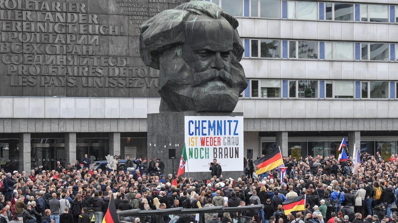 Teilnehmer der Kundgebung der rechtspopulistischen Bürgerbewegung Pro Chemnitz versammeln sich vor dem Karl-Marx-Denkmal, an dem immer noch ein Plakat des Bündnisses Chemnitz Nazifrei hängt. Teilnehmer der Kundgebung der rechtspopulistischen Bürgerbewegung Pro Chemnitz versammeln sich vor dem Karl-Marx-Denkmal, an dem immer noch ein Plakat des Bündnisses Chemnitz Nazifrei hängt.