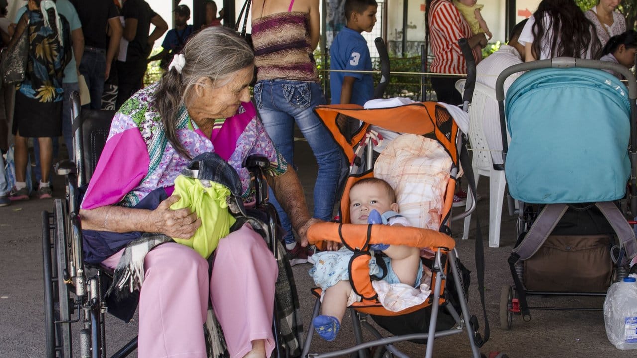 Eine ältere venezolanische Frau im Rollstuhl schaut auf ihr Enkelkind, während die Mutter des Kindes einen Arzt holt.