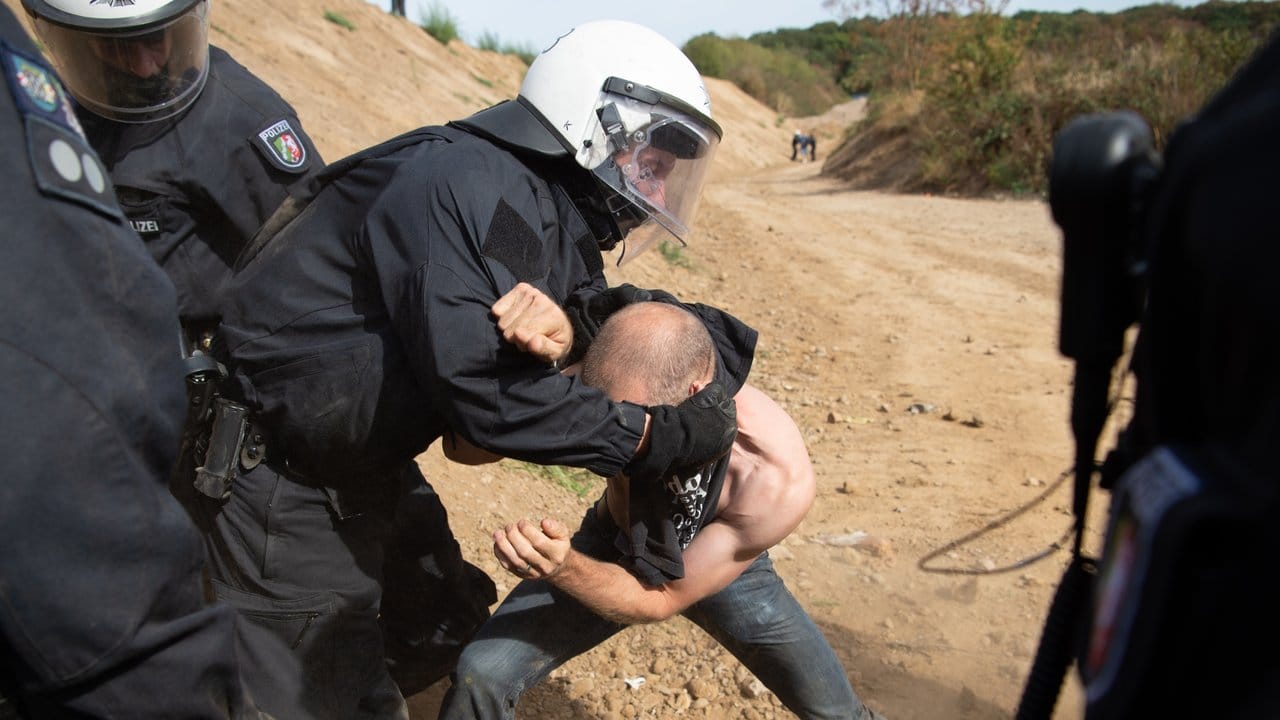 Ein Teilnehmer einer Demonstration wird von der Polizei daran gehindert, über einen Wall in den Wald zu kommen.