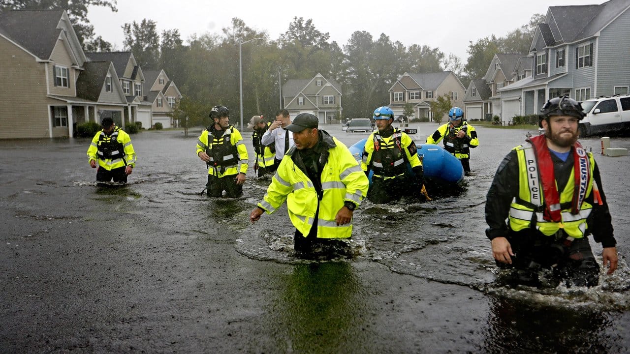 Mitglieder eines Rettungsteams waten durch überschwemmte Straßen auf der Suche nach Bewohnern.