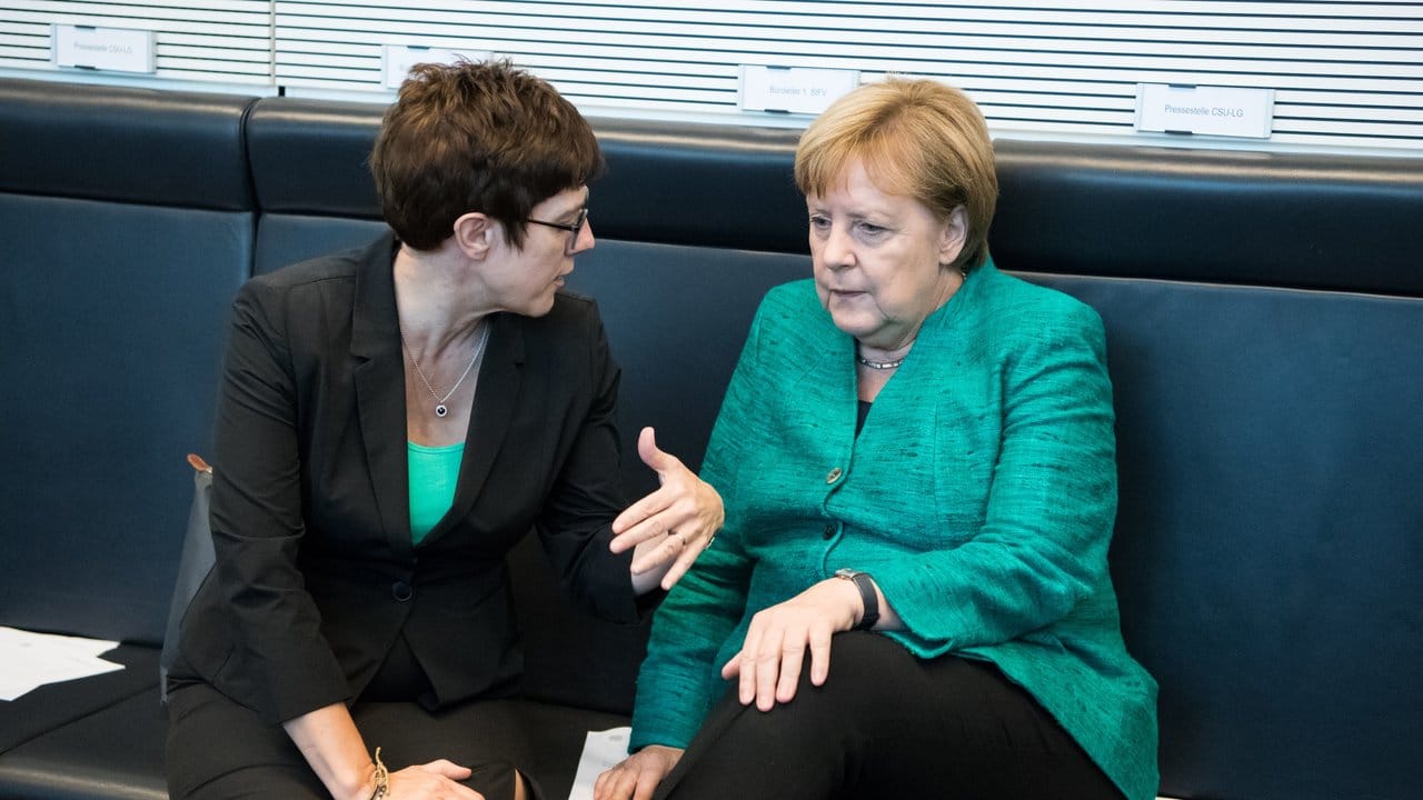 CDU-Generalsekretärin Kramp-Karrenbauer (l) und Kanzlerin Merkel unterhalten sich im Bundestag.