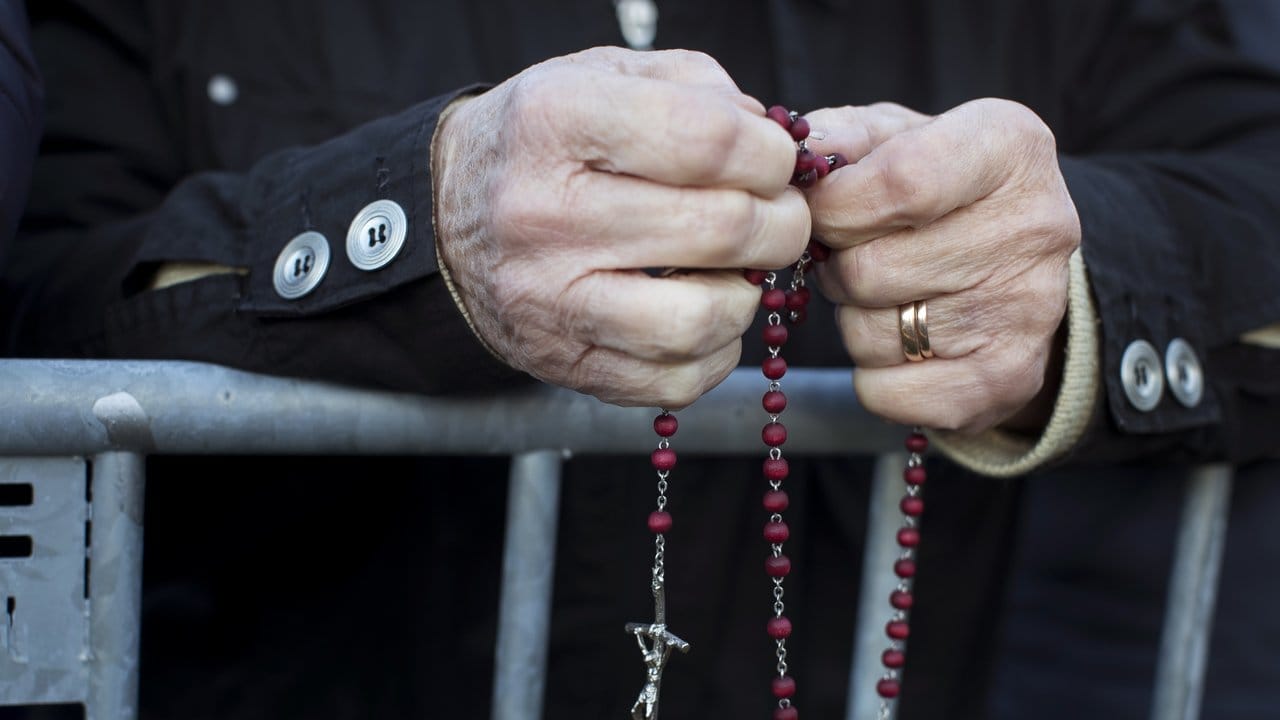 Eine Frau betet mit einem Rosenkranz in den Händen, während sie auf die Ankunft von Papst Franziskus wartet.