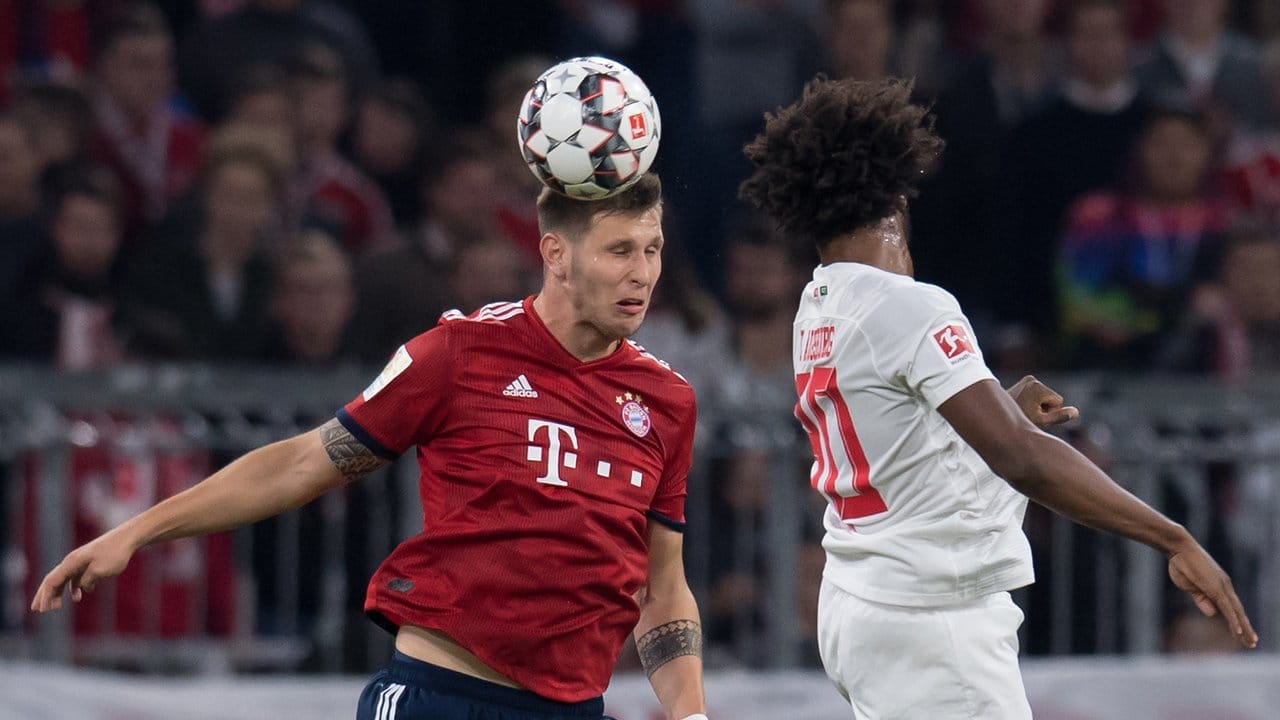 Die Bayern um Niklas Süle (l), hier im Kopfballduell mit dem Augsburger Caiuby, bleiben trotz des 1:1 Spitzenreiter.