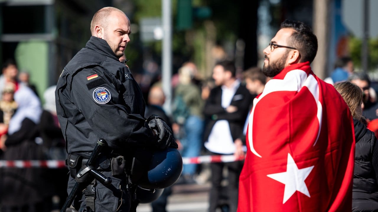 Ein Polizist und eine Erdogan-Anhänger mit einer türkischen Flagge stehen an einer Absperrung im Umfeld der Ditib-Zentralmoschee in Köln.