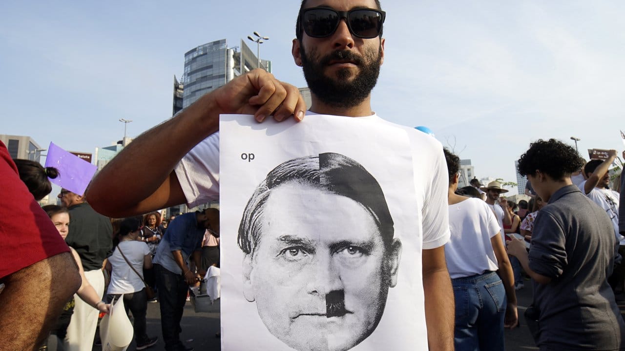 Ein Mann hält ein Plakat hoch, auf dem der rechtsextreme Präsidentschaftskandidat Bolsonaro ein Hitlerbärtchen hat.