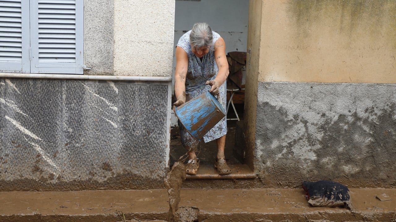 Eine Anwohnerin befreit nach einem schweren Unwetter ihr Haus von Schlamm und Trümmern. Eine Anwohnerin befreit nach einem schweren Unwetter ihr Haus von Schlamm und Trümmern.