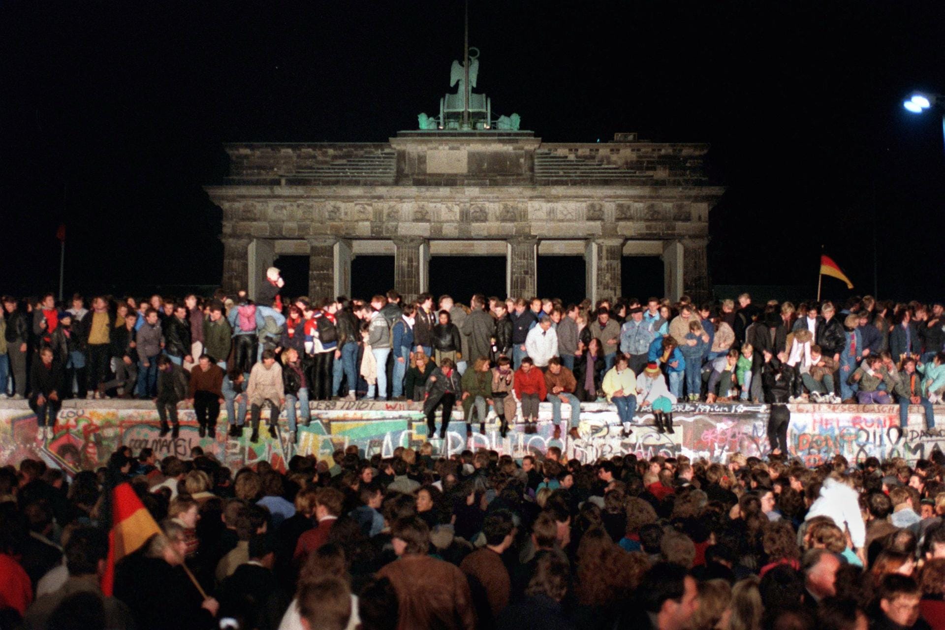 Jubelnde Menschen stehen auf der Berliner Mauer am Brandenburger Tor. Der 30. Jahrestag des Mauerfalls macht Deutschland zu einem interessanten Reiseziel im kommenden Jahr.