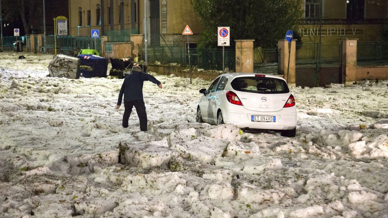 Ein Mann versucht in Rom ein durch Hagelmassen blockiertes Auto zu erreichen.