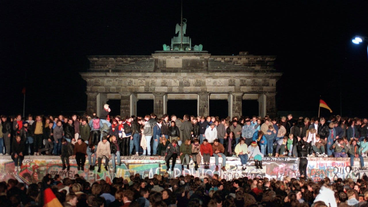 Vor 29 Jahren: Jubelnde Menschen sitzen auf der Berliner Mauer am Brandenburger Tor.