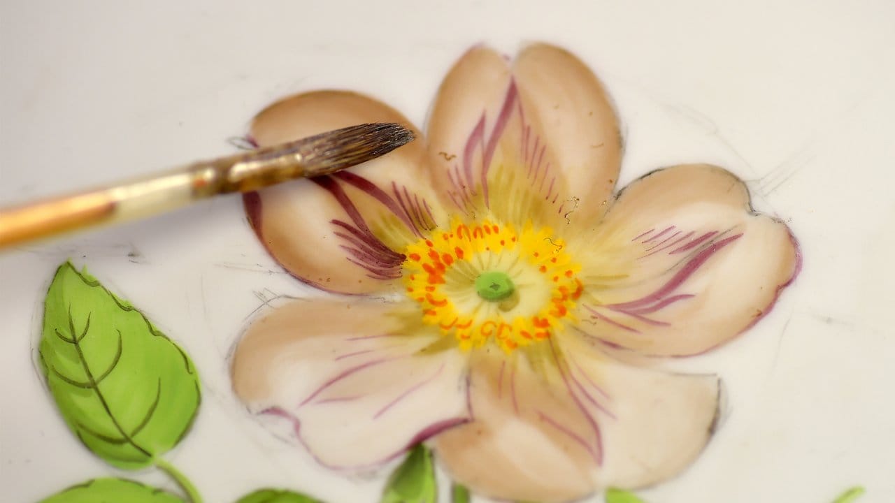 Ein feines Blumenmuster ziert einen Teller: Manufakturporzellanmaler tragen solche Dekore mit feinen Pinseln auf Keramikgeschirr auf.