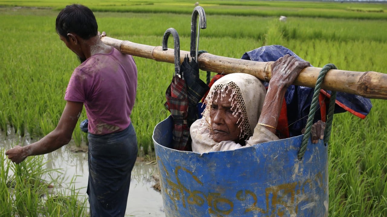 Flüchtlinge der Rohingya tragen eine alte Frau über einen schlammigen Weg, nachdem sie die Grenze zwischen Bangladesch und Myanmar überquert haben.