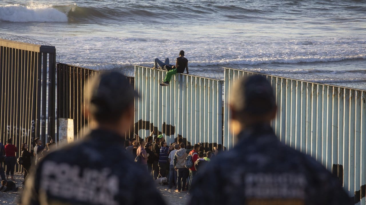 Zwei mexikanische Polizisten beobachten bei Tijuana Migranten am Grenzzaun zu den USA.