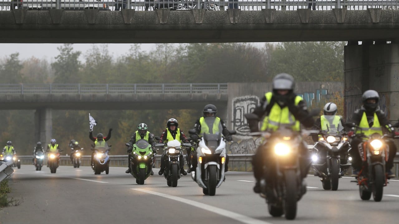 Demonstranten stehen auf einer Brücke, während Motorradfahrer mit gelben Westen auf der Straße unterwegs sind, um gegen die Spritpreise zu protestieren.