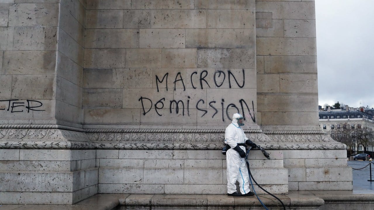 "Macron Rücktritt": Ein Arbeiter der Stadtreinigung beseitigt Grafitti von einer Wand des Arc de Triomphe in Paris.