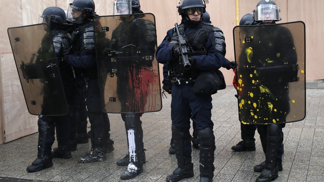 Schwarz-bunt: Polizisten mit farbverschmierten Schutzschildern beobachten den Protest der "Gilets Jaunes" in Paris.