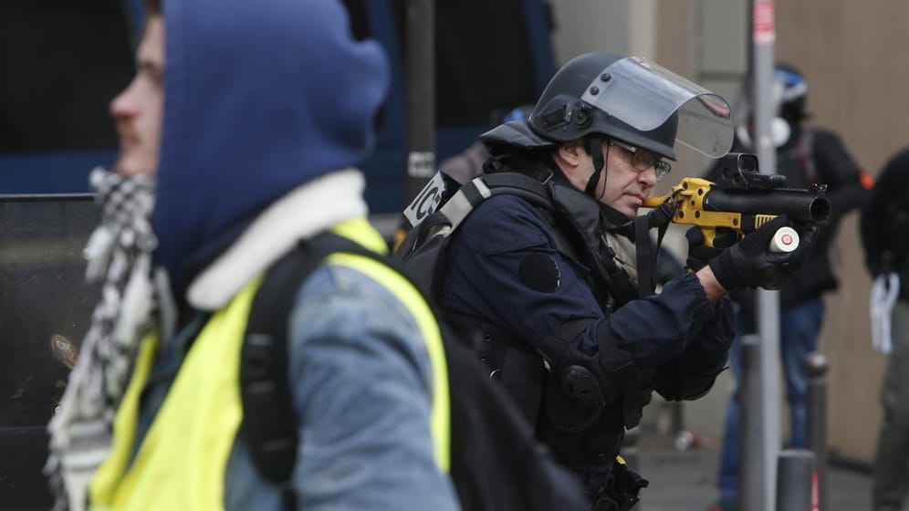 Ein Polizist legt auf den Champs-Elysees eine Tränengaspistole an.