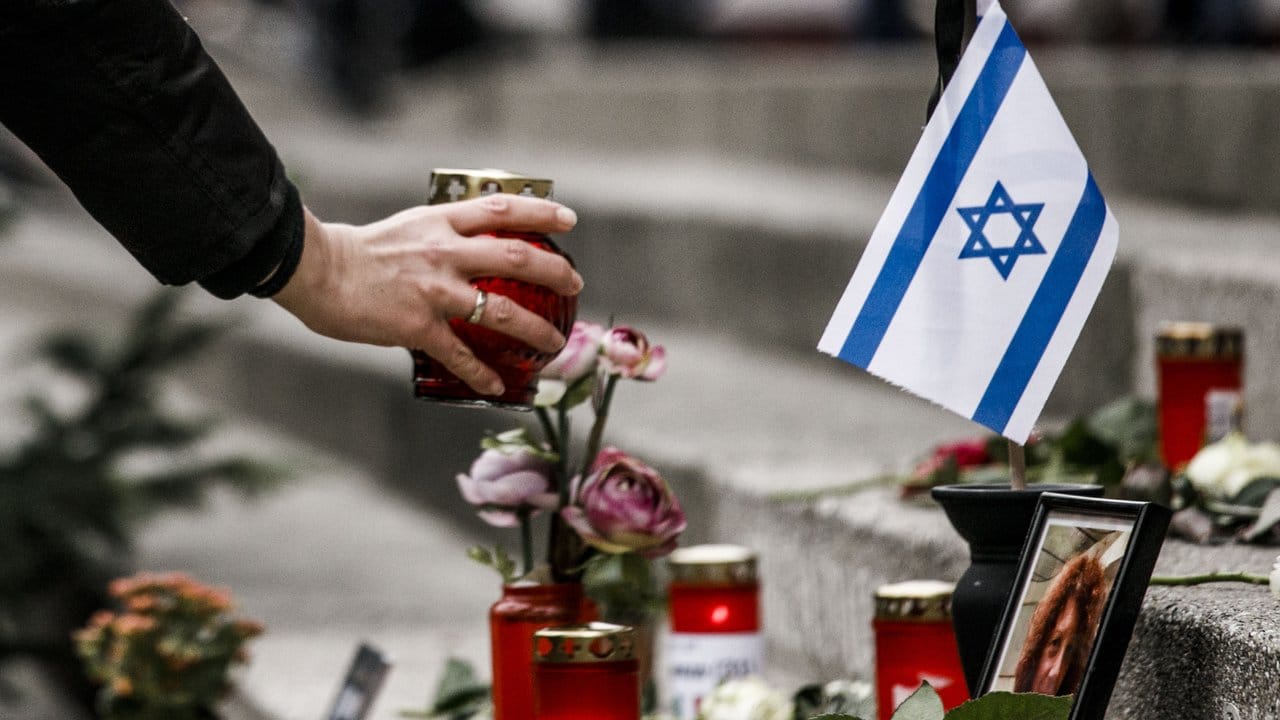 Eine Frau zündet am Breitscheidplatz am Mahnmal vor einer israelischen Fahne ein Kerzenlicht ab.