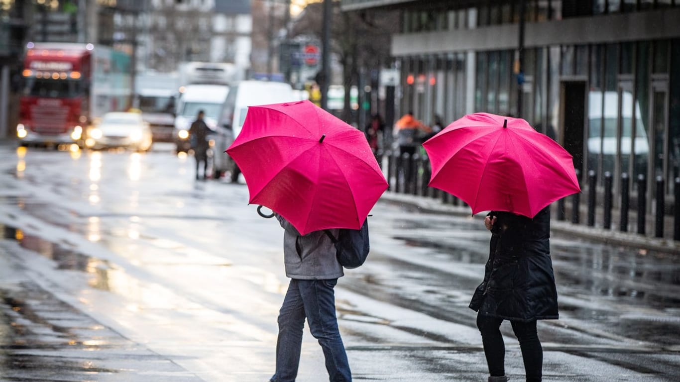 Kleiner Farbtupfer: Passanten mit Regenschirmen überqueren bei Wind und Regen eine Kreuzung in der Frankfurter Innenstadt.