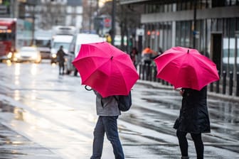 Kleiner Farbtupfer: Passanten mit Regenschirmen überqueren bei Wind und Regen eine Kreuzung in der Frankfurter Innenstadt.