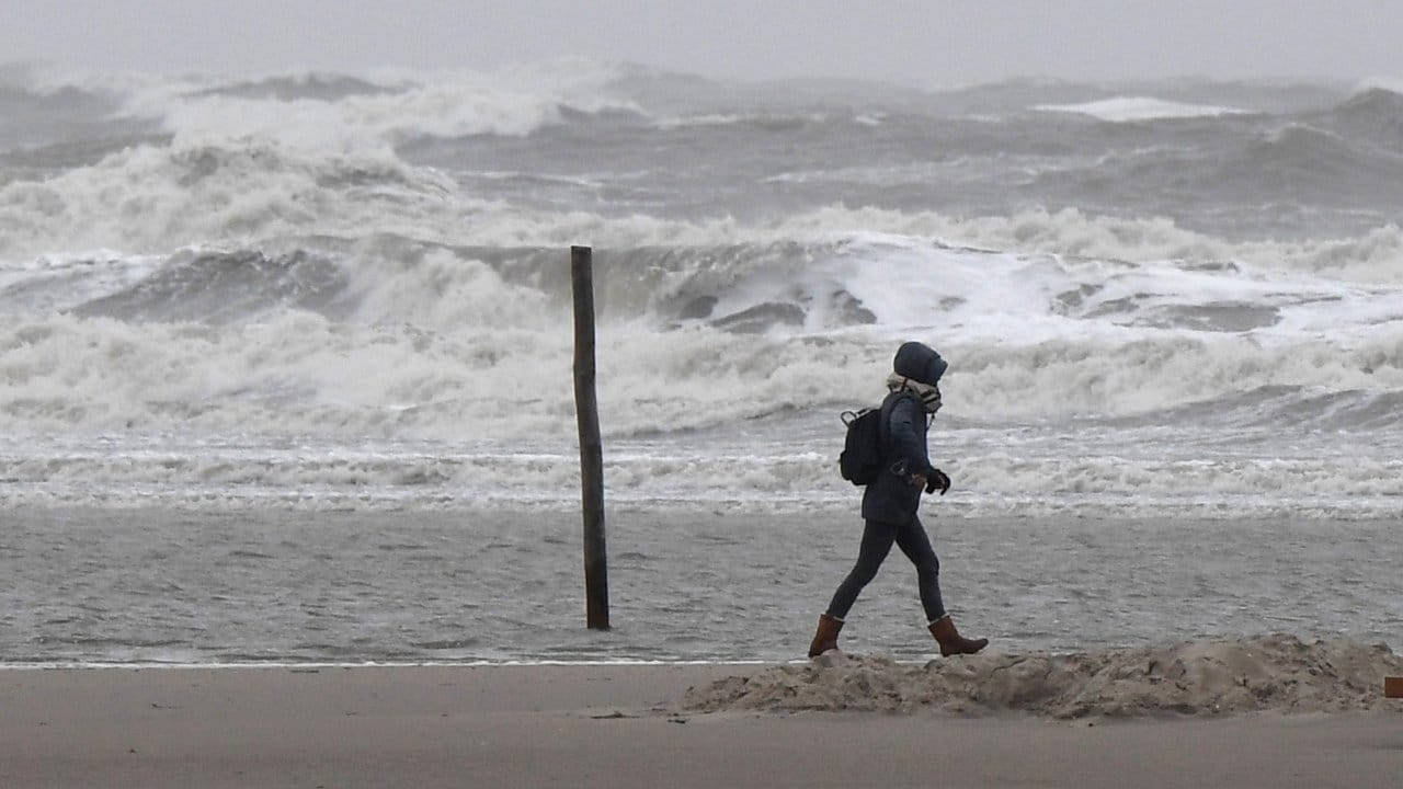Eine Spaziergängerin geht im Sturm über den Nordseestrand.