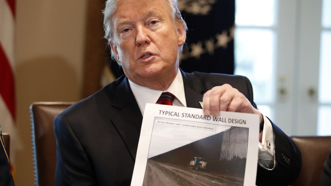 Donald Trump hält ein Foto einer möglichen Grenzmauer in der Hand.