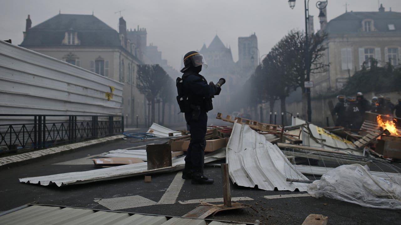 Ein Polizist in Schutzkleidung auf einer Straße in Bourges, umgeben von Trümmern einer Barrikade.