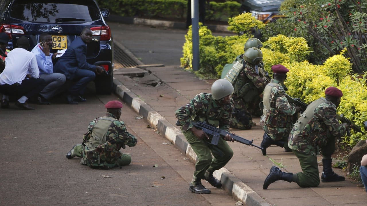 Kenianische Streitkräfte suchen hinter Büschen und Autos Schutz.