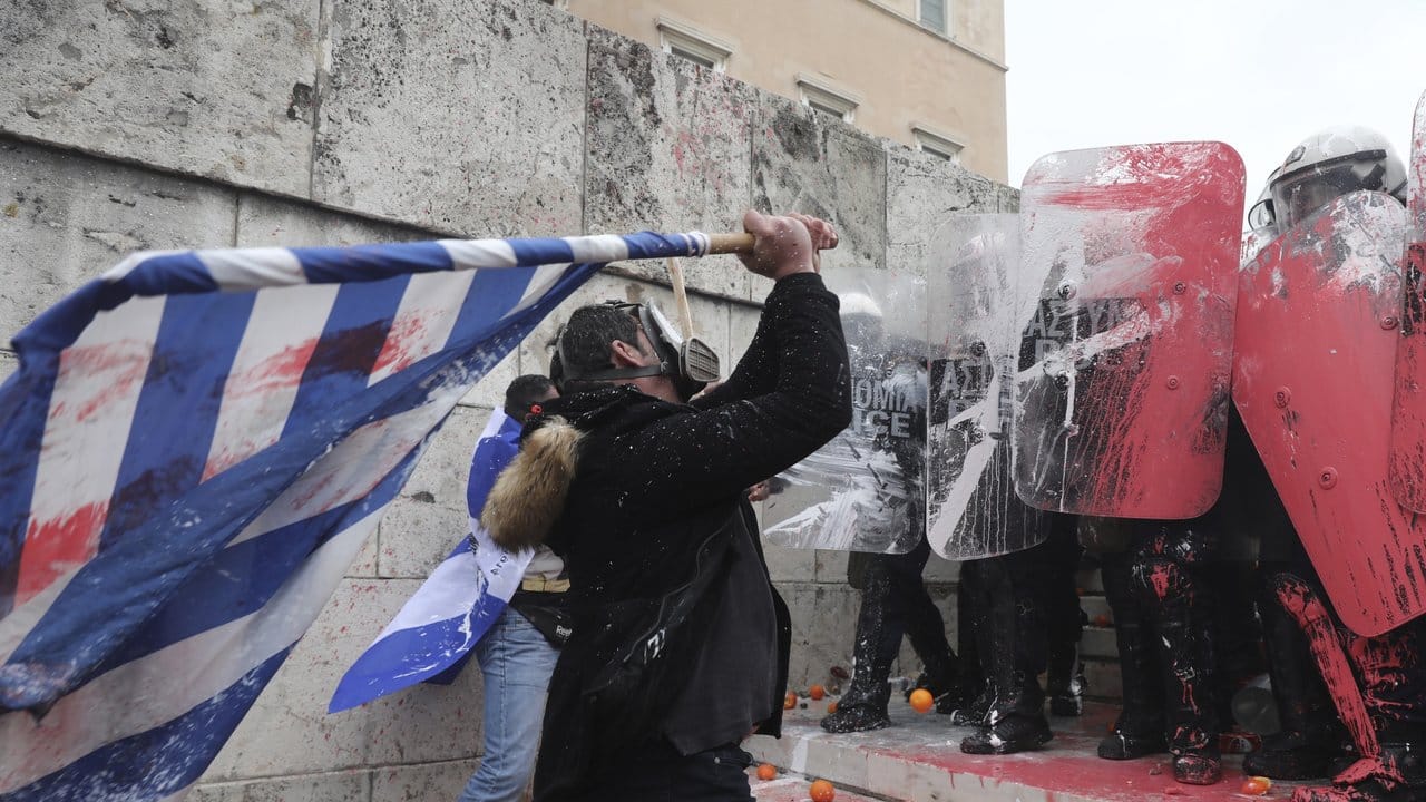 Ein maskierter Demonstrant schlägt mit mit einer griechischen Flagge auf Bereitschaftspolizisten ein. Ein maskierter Demonstrant schlägt mit mit einer griechischen Flagge auf Bereitschaftspolizisten ein.