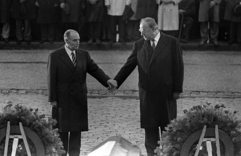 Hände halten für den Frieden:1984 besuchen der deutsche Bundeskanzler Helmut Kohl und der französische Staatspräsident François Mitterrand einen deutschen Soldatenfriedhof. Während einer Feierstunde zum Gedenken an die Gefallenen beider Weltkriege streckt Mitterrand die Hand nach Kohl aus, der ergreift diese. Das Bild geht als Symbol der Versöhnung in die Geschichte ein.