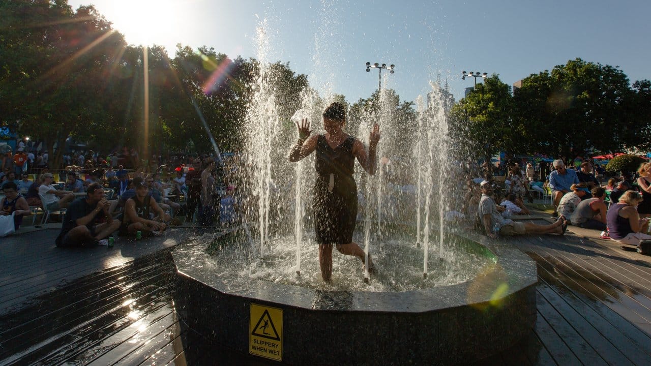 Eine Frau erfrischt sich in kompletter Kleidung in einem Brunnen im Melbourne Park ab.