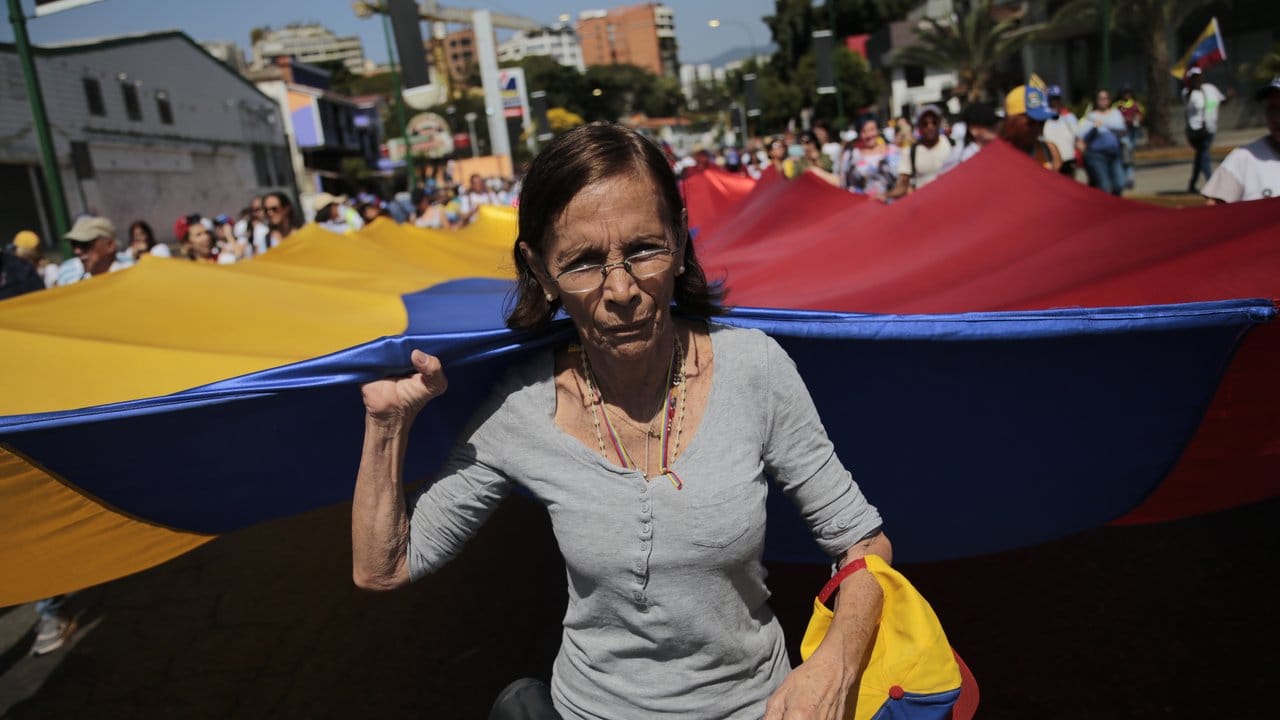 Eine Frau trägt bei der Protestkundgebung der Opposition gemeinsam mit anderen Demonstranten eine große venezolanische Flagge.