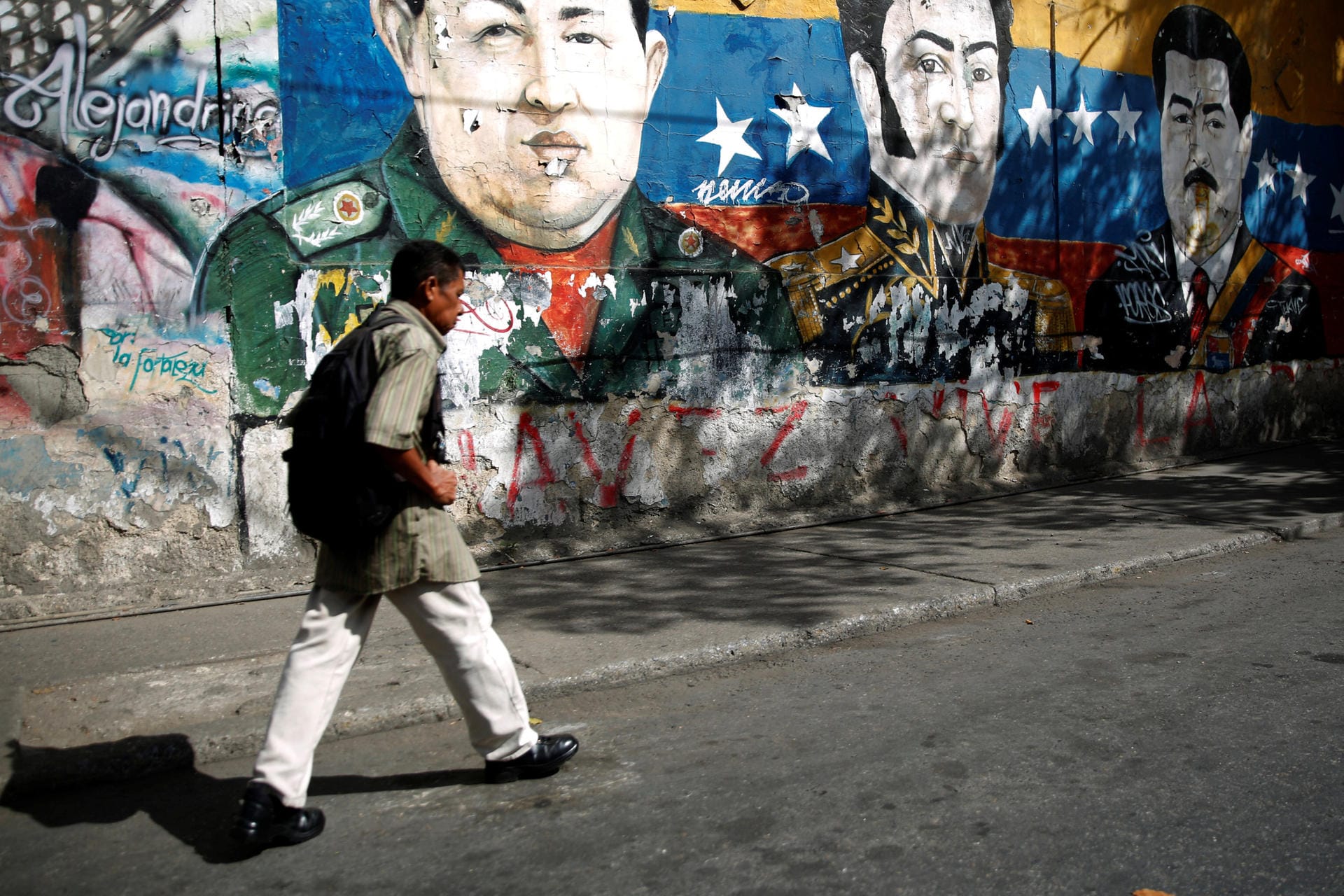 A man walks by graffiti of South American revolutionary hero Simon Bolivar, Venezuela's late President Hugo Chavez and Venezuela's President Nicolas Maduro at the Jose Felix Ribas neighborhood in Caracas