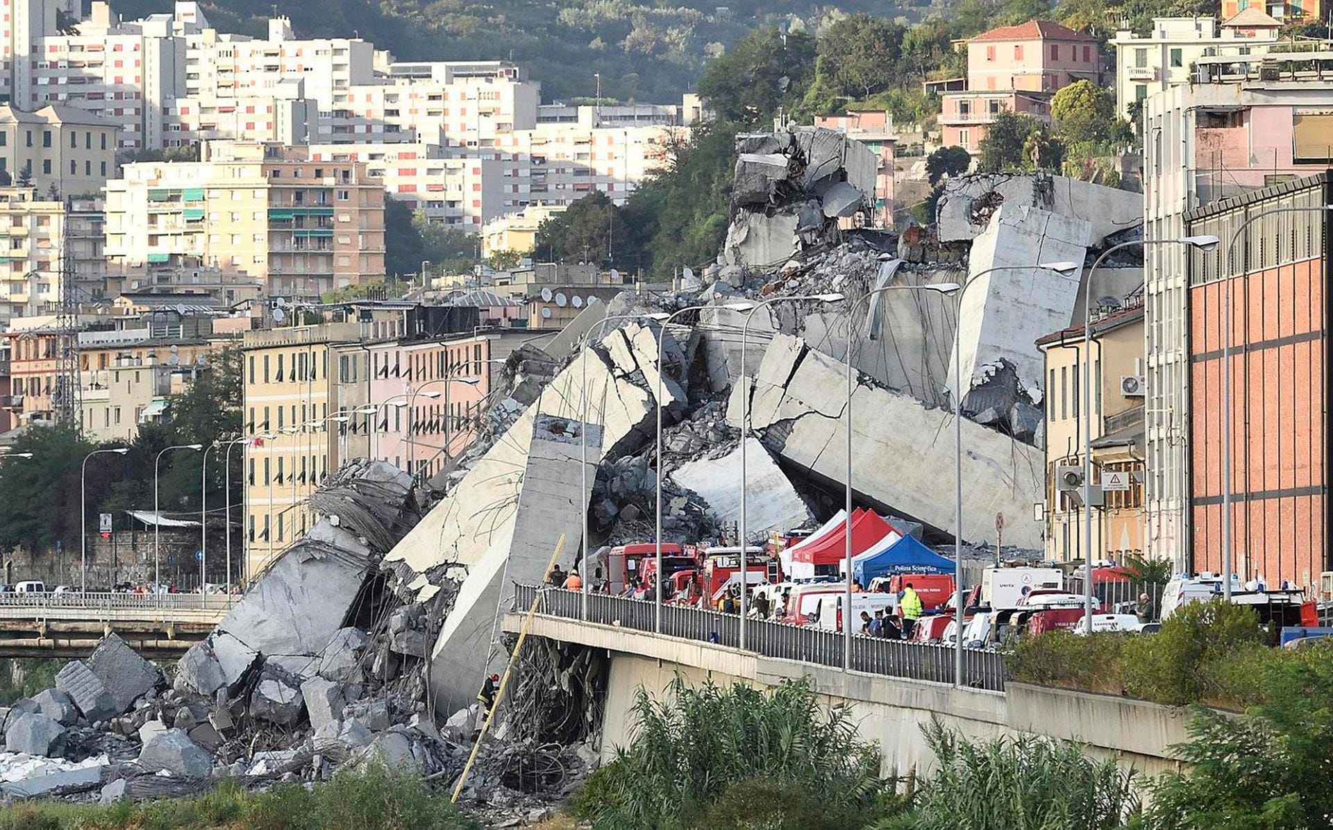 Fahrzeuge der Rettungskräfte stehen vor der teilweise eingestürzten Autobahnbrücke. Der Einsturz der Ponte Morandi erfolgte auf etwa 100 Metern Länge.