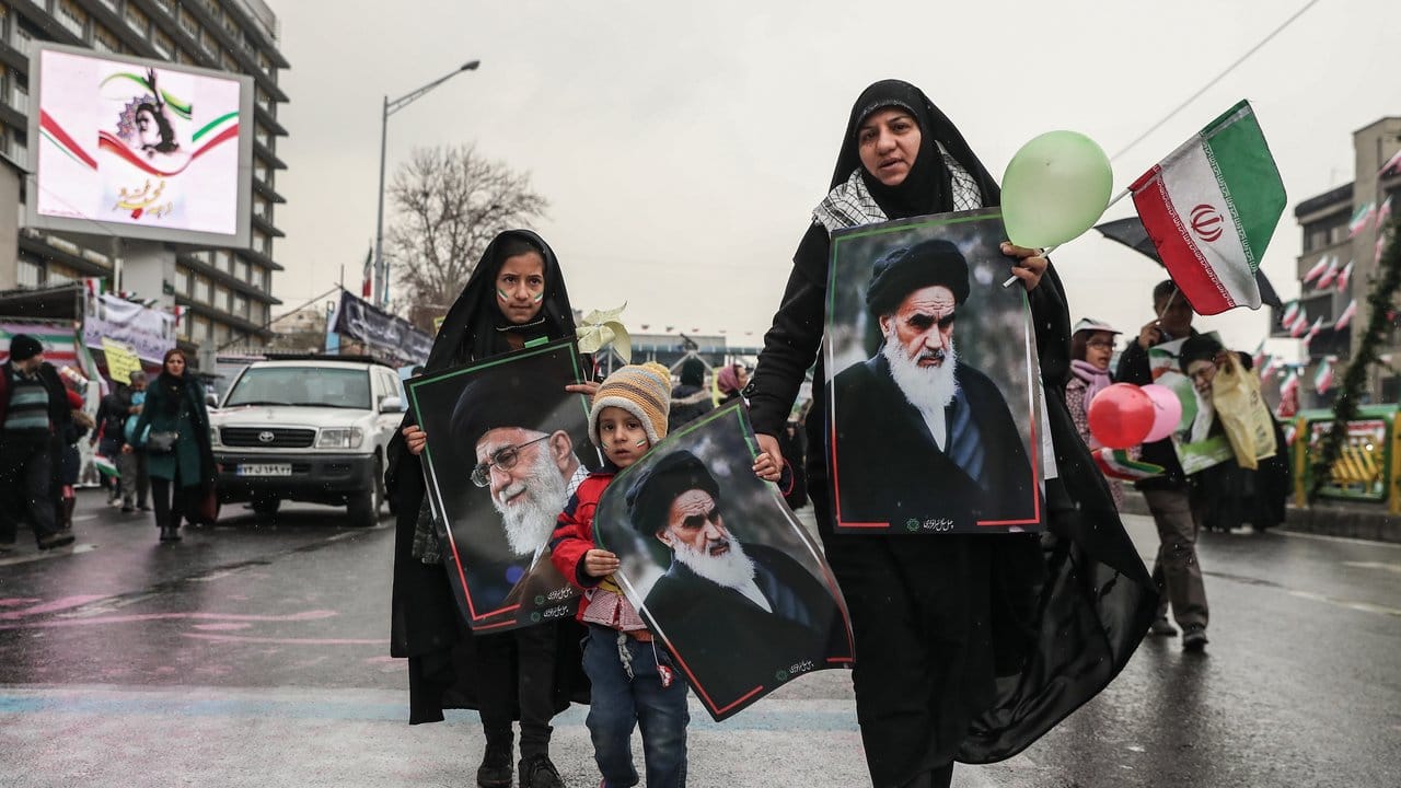 Eine Frau und ihre Kinder halten in Teheran Bilder von Ajatollah Ruhollah Chomeini.