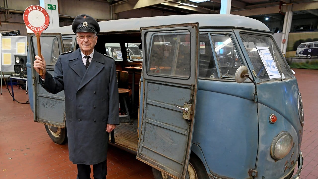 Heinz Scholze in historischer Uniform und mit Winkerkelle vor einem 66 Jahre alten T1 VW-Bulli in der Oldtimersammlung von VW-Nutzfahrzeuge.