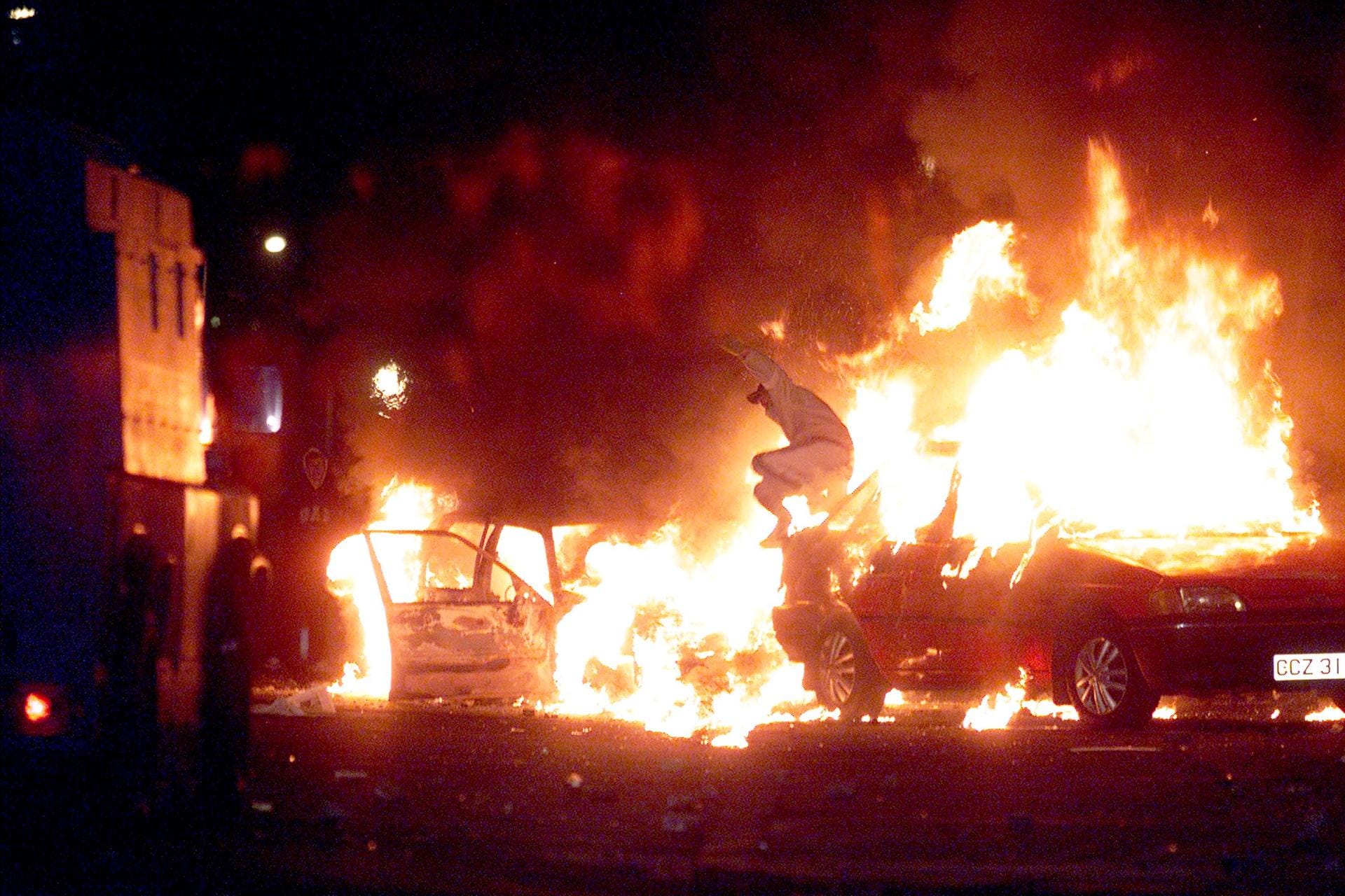 Gewaltausbrüche im Jahr 2002: Ein Mann springt über ein brennendes Auto. Zuvor waren Konflikte zwischen ethnisch-religiösen Gruppen wieder aufgeflammt.