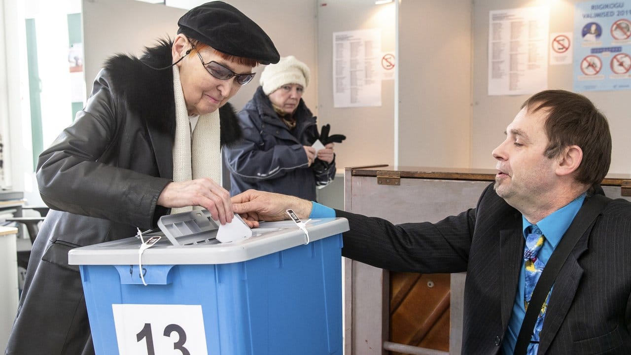 Ein Mitarbeiter der Wahlkommission hilft in einem Wahllokal in Tallinn einer Frau bei der Stimmabgabe.