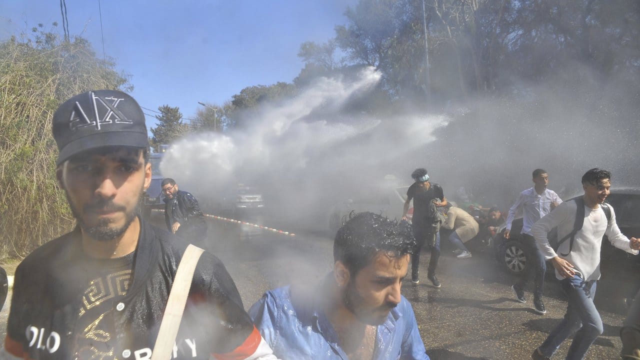 Demonstranten gehen in Algier vor einem Wasserwerfer der Polizei in Deckung.