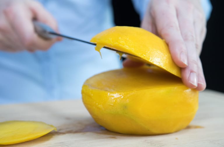 Mango: Schritt 3 – Die Mango auf die nun flache Seite legen. Dann von der oberen, gewölbten Seite eine weitere Scheibe Fruchtfleisch abschneiden.